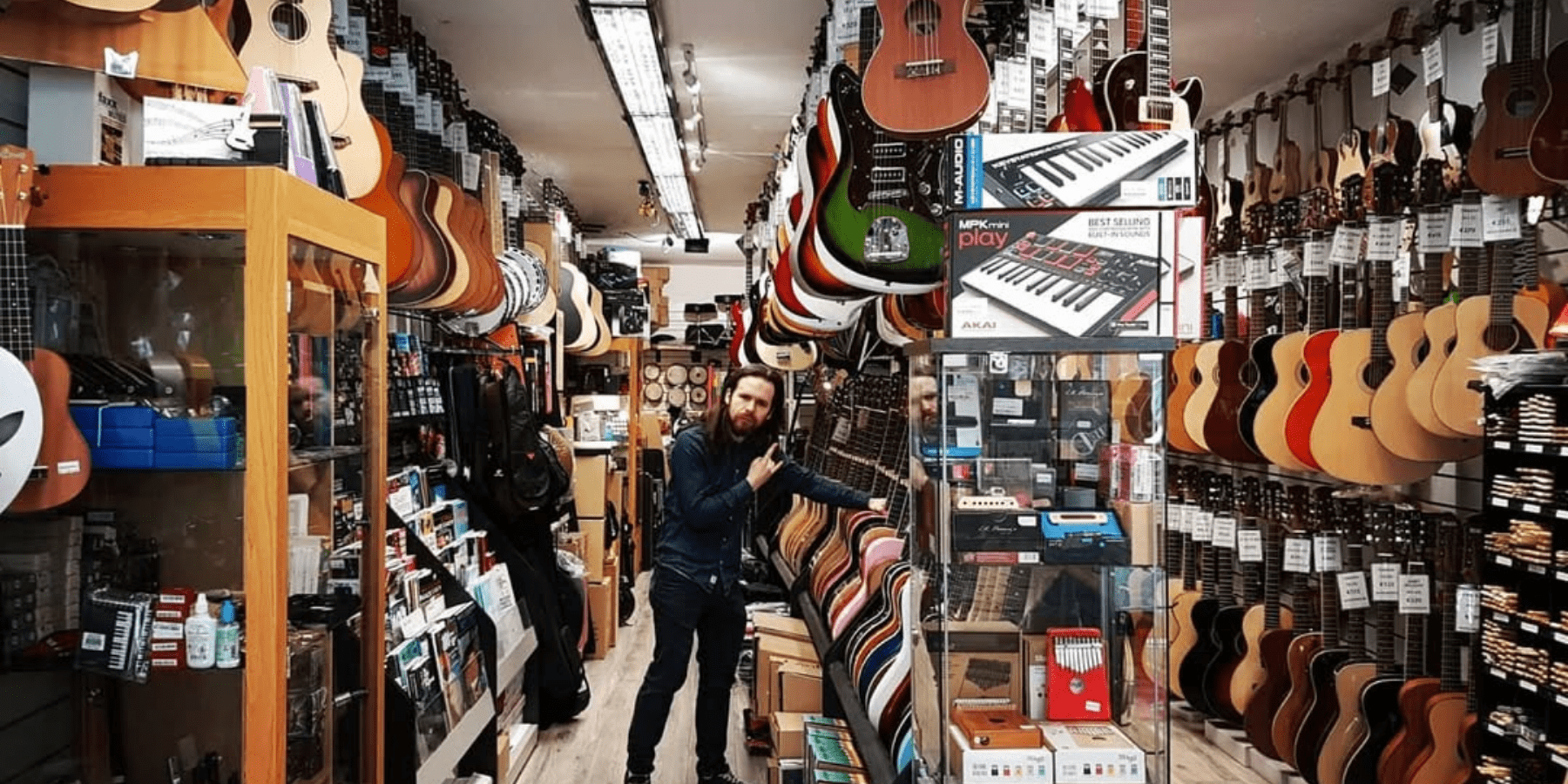 Man standing in the middle of three rows of guitars.
