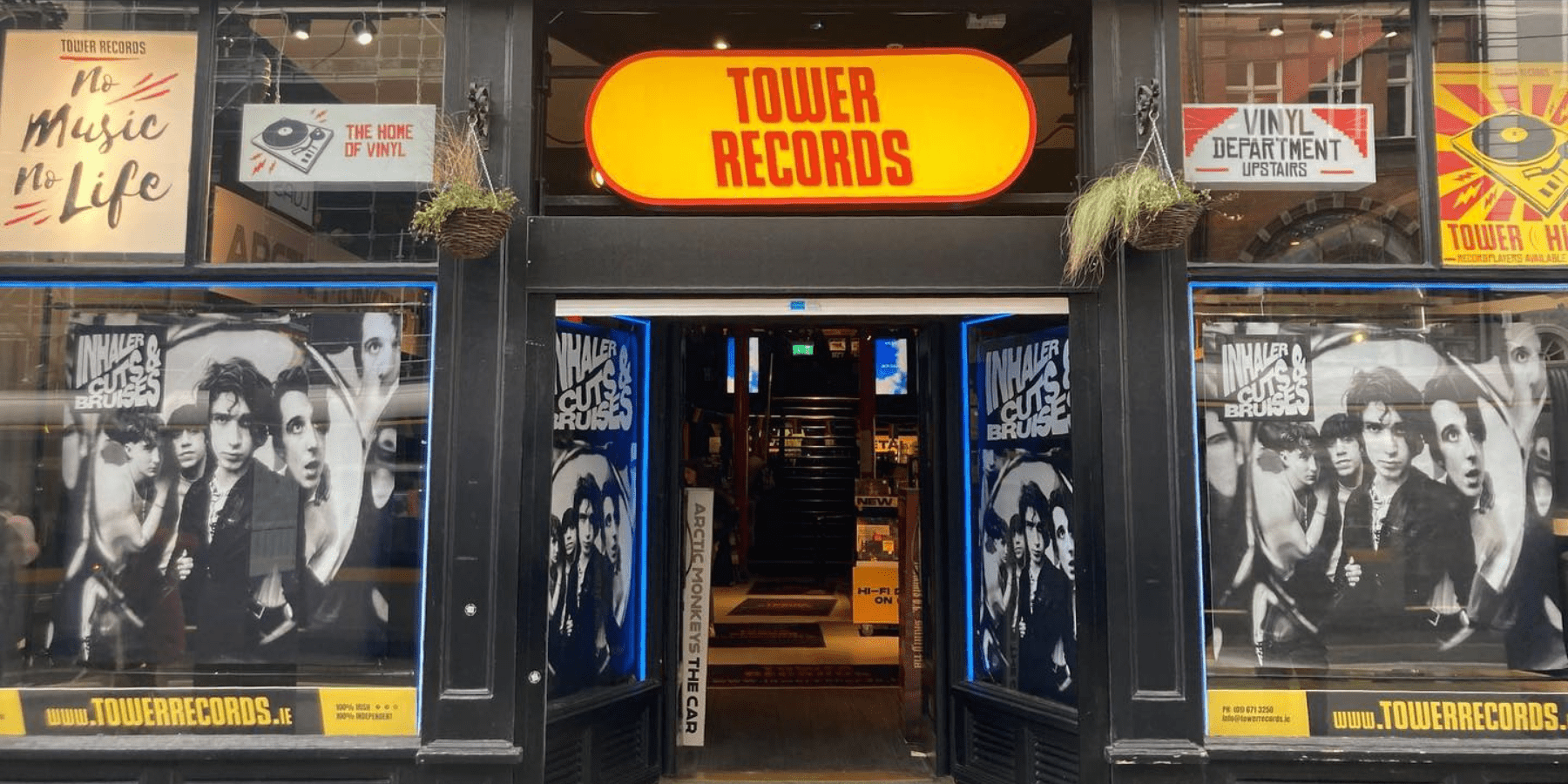 The store-front of Tower Records. It has a bright yellow sign and posters of a musical artist in the window.